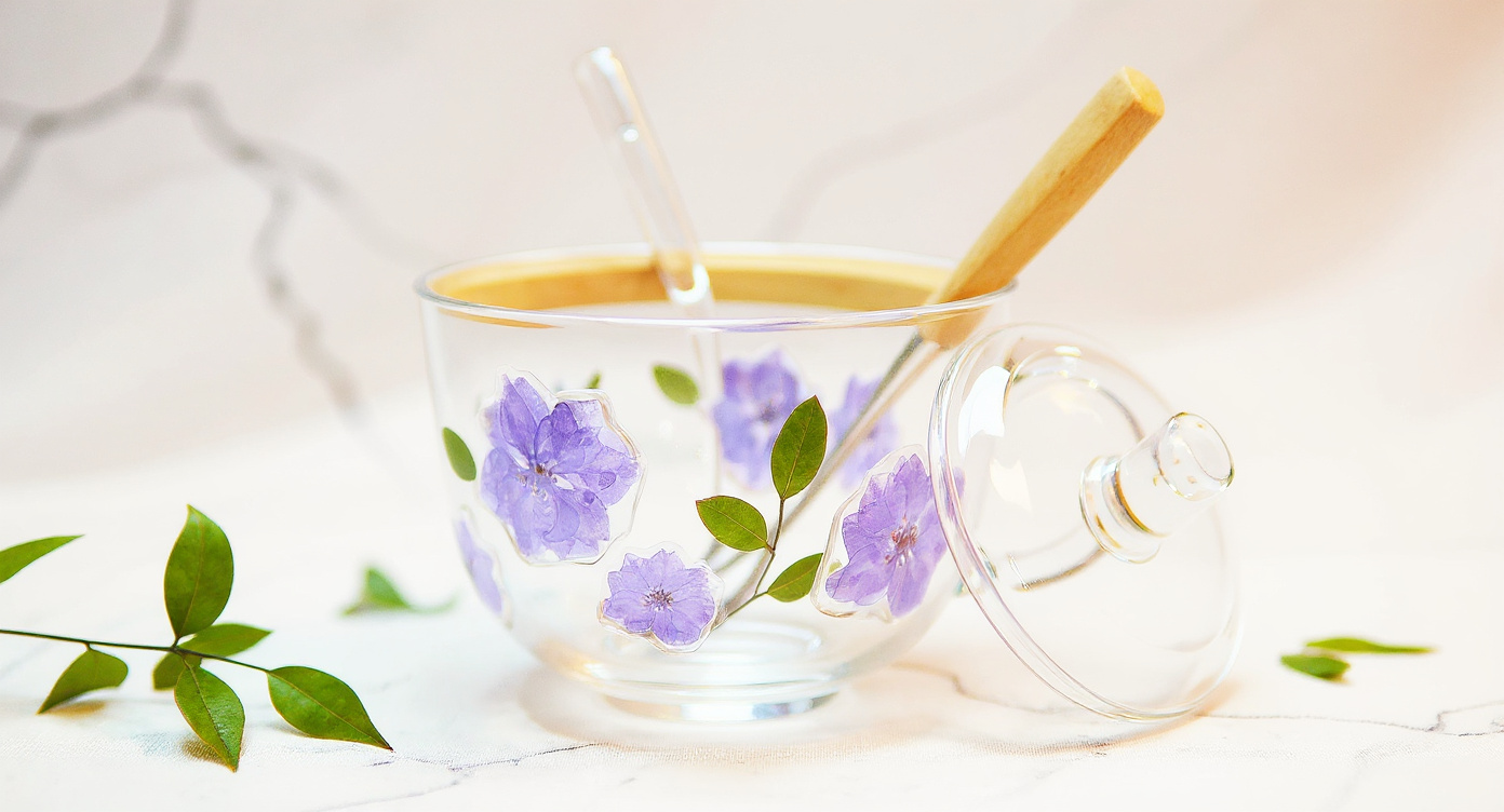 Handcrafted Floral Glass Cup with Real Preserved Flowers holding iced coffee, glass straw and lid on marble