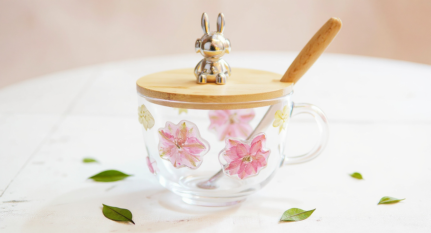 Handcrafted Floral Glass Cup with Real Preserved Flowers, lid, straw on marble flat lay.