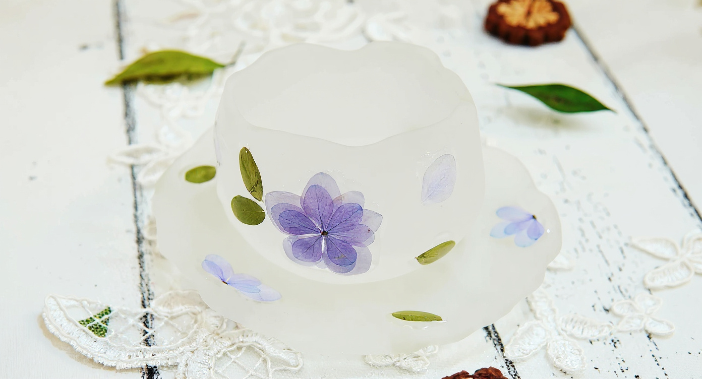 Frosted glass teacup with real blue hydrangea and matching saucer on aged oak board.