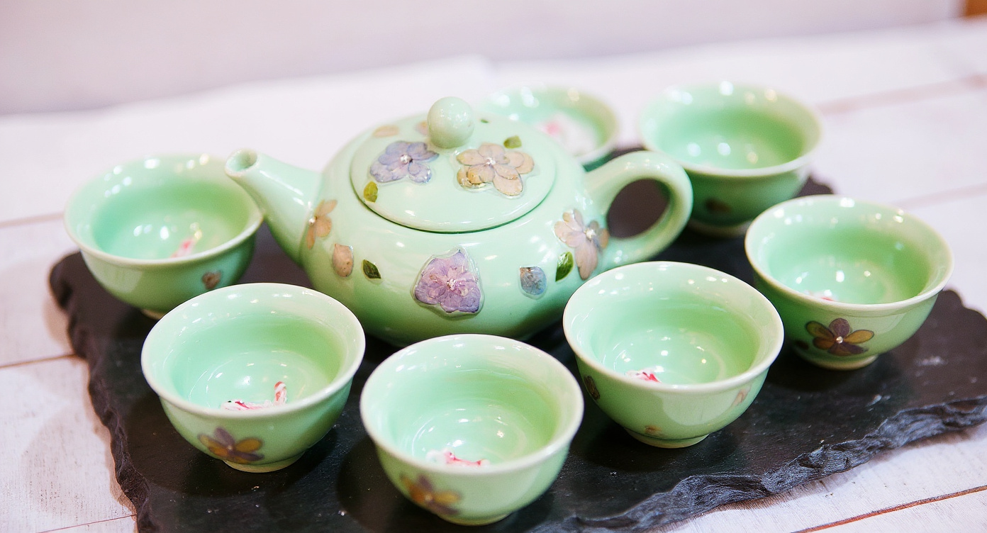 Celadon cup with 3D koi fish visible under tea on bamboo mat.