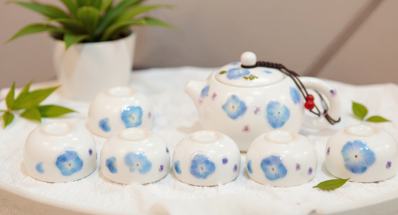 Handmade Porcelain Tea Set with blue hydrangeas beside glass teapot of blooming floral tea.