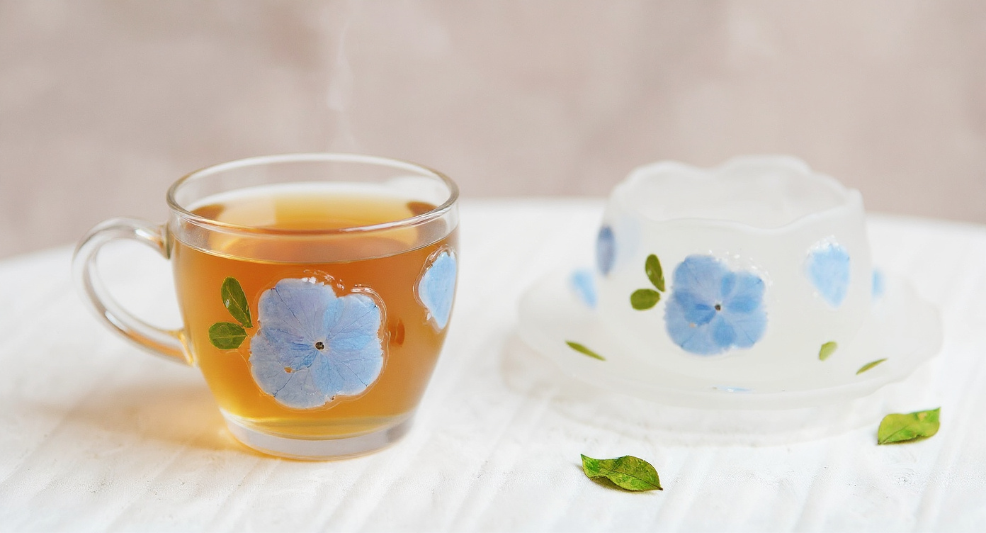Handmade glass teacup set with preserved hydrangea on ceramic tray flat lay
