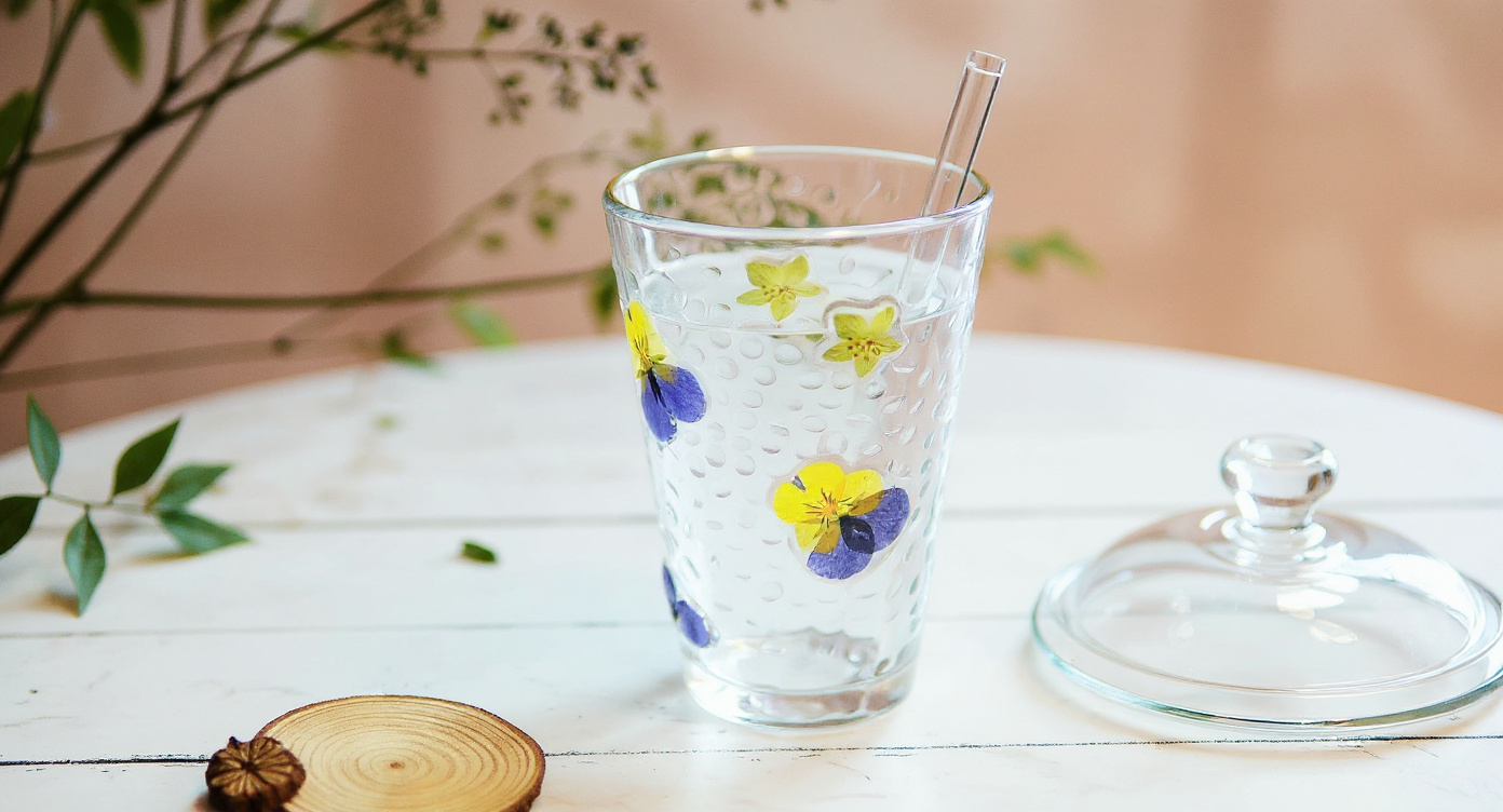 Handmade Floral Glass Cup with iced coffee and glass straw beside small floral vase.