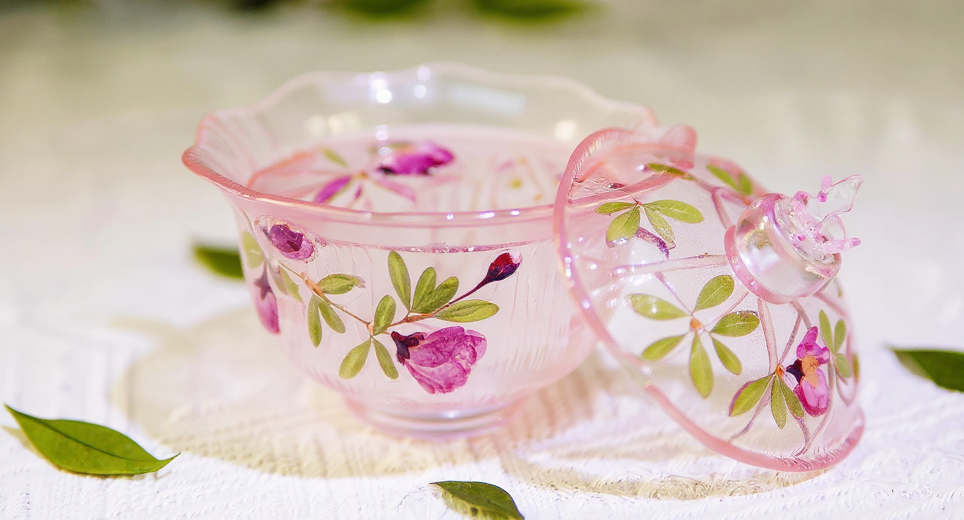 Handmade gradient pink butterfly glass cup with iced botanical tea and matching lid on linen