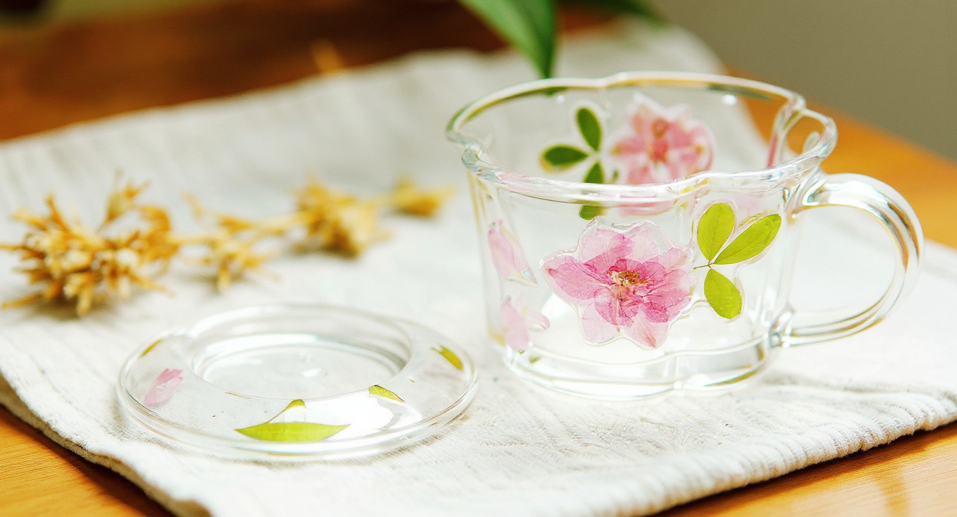 Pressed Flower Glass Cup & Saucer with vintage books and silver teaspoon on wood.